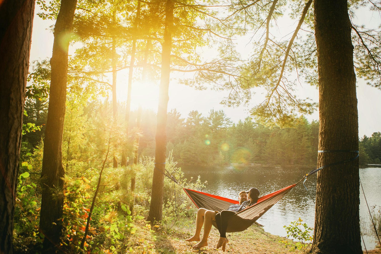 Two people relaxing in a hammock by a lake at sunset